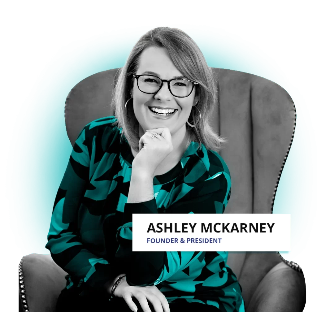 Ashley, founder and president of Involvi, wears a teal and black patterned blouse, sitting in an office chair and smiling at the camera.