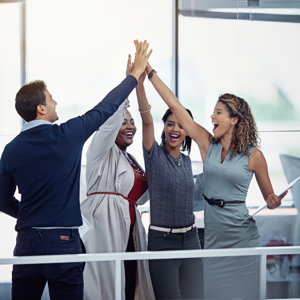 A group of colleagues high fiving together in an office.